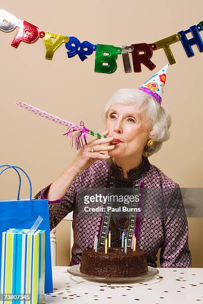 senior woman celebrating birthday, indoors - matasuegras fotografías e imágenes de stock