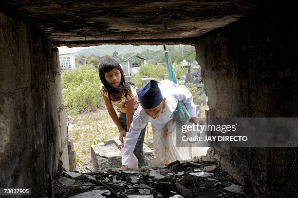 Siquijor, PHILIPPINES: An elderly woman and her grandaughter gather ashes from a tomb in Siquijor island cemetery, located in the central...