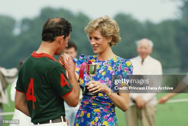 Princess Diana , wearing a Belville Sassoon dress, presenting Prince Charles with a trophy after competing at the Hola Cup polo match at the Guards...
