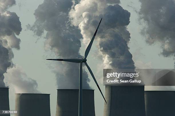 Loan wind turbine spins as exhaust plumes from cooling towers at the Jaenschwalde lignite coal-fired power station, which is owned by Vatenfall,...