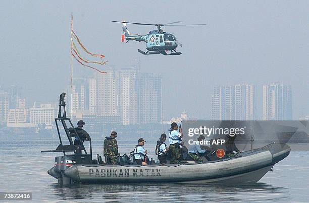 Indonesian Navy Special Forces Frogman and Singapore clearance divers sit aboard a speed boat as an Indonesian Navy helicopter passes above during a...