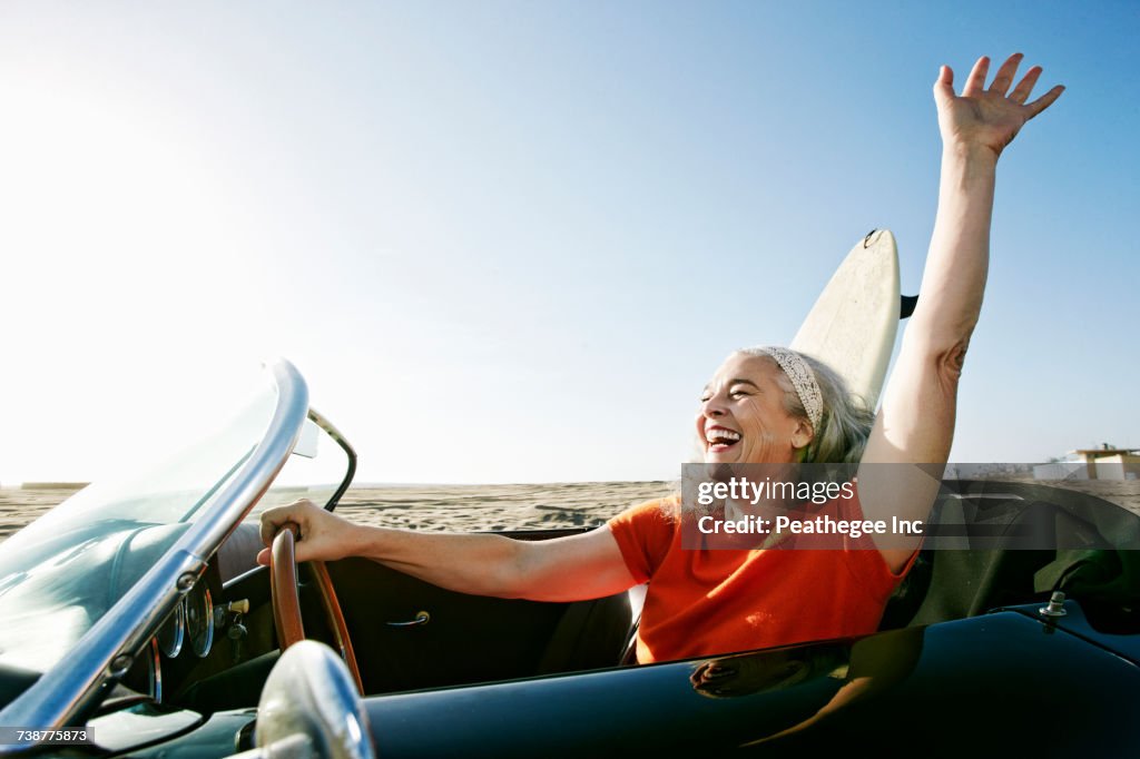 Older Caucasian woman in convertible car with surfboard on beach