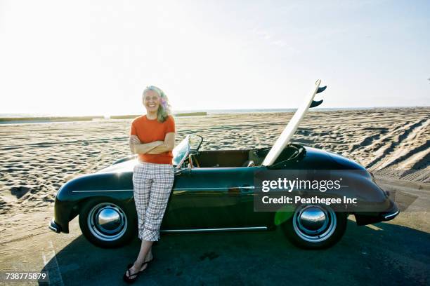 older caucasian woman leaning on convertible car with surfboard on beach - man lean car stock-fotos und bilder