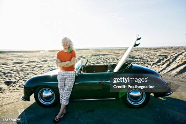 older caucasian woman leaning on convertible car with surfboard on beach - manhattan beach stock pictures, royalty-free photos & images