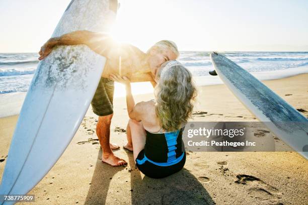 older caucasian couple on beach with surfboards kissing - chest kissing stockfoto's en -beelden