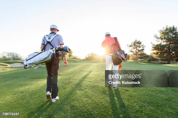 men carrying golf bags on sunny golf course - golf bag stock pictures, royalty-free photos & images