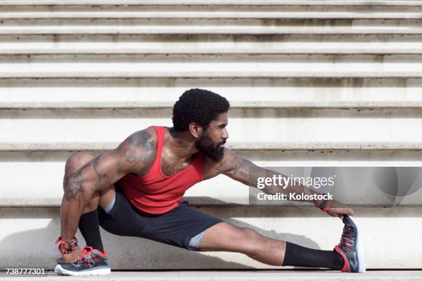 african american man stretching leg on bleachers - touch toes stock-fotos und bilder