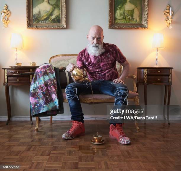 fashionable older caucasian man with beard sitting on bench pouring tea - versierd jak stockfoto's en -beelden