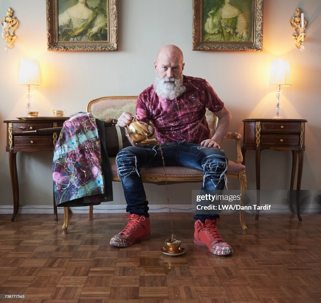 Fashionable older Caucasian man with beard sitting on bench pouring tea