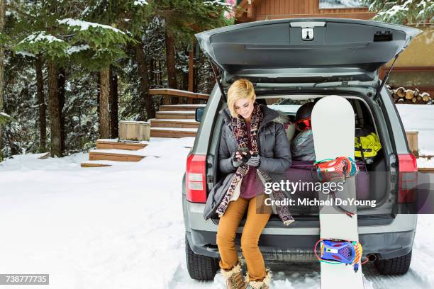 caucasian woman at car texting on cell phone in winter - loader reading stock pictures, royalty-free photos & images