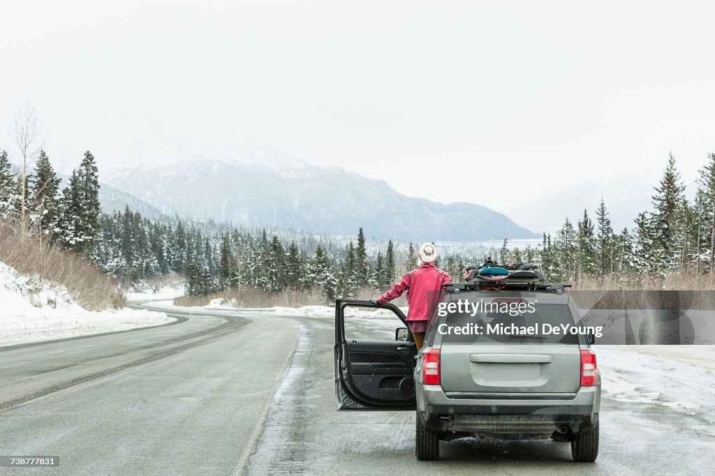 Caucasian woman standing in car in winter admiring scenic view