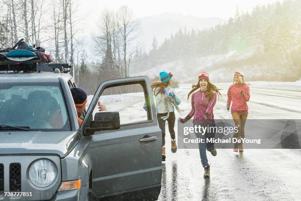 women running to car in winter - carro de corrida fotografías e imágenes de stock