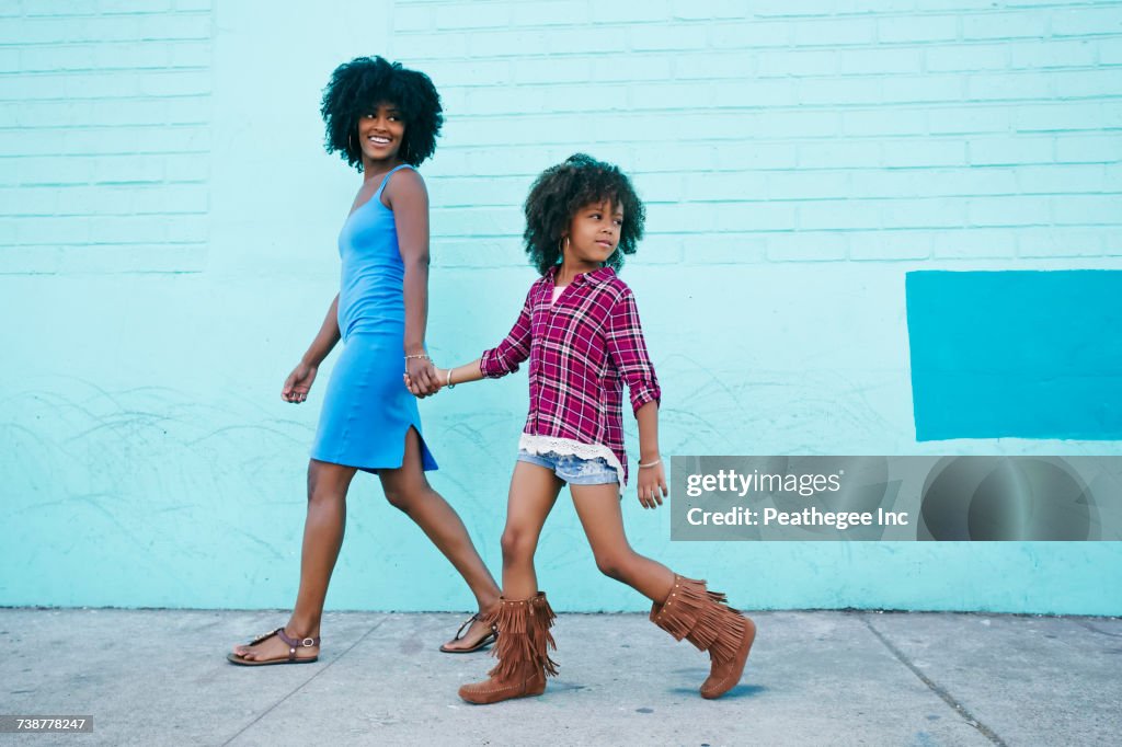 Smiling mother and daughter walking on sidewalk