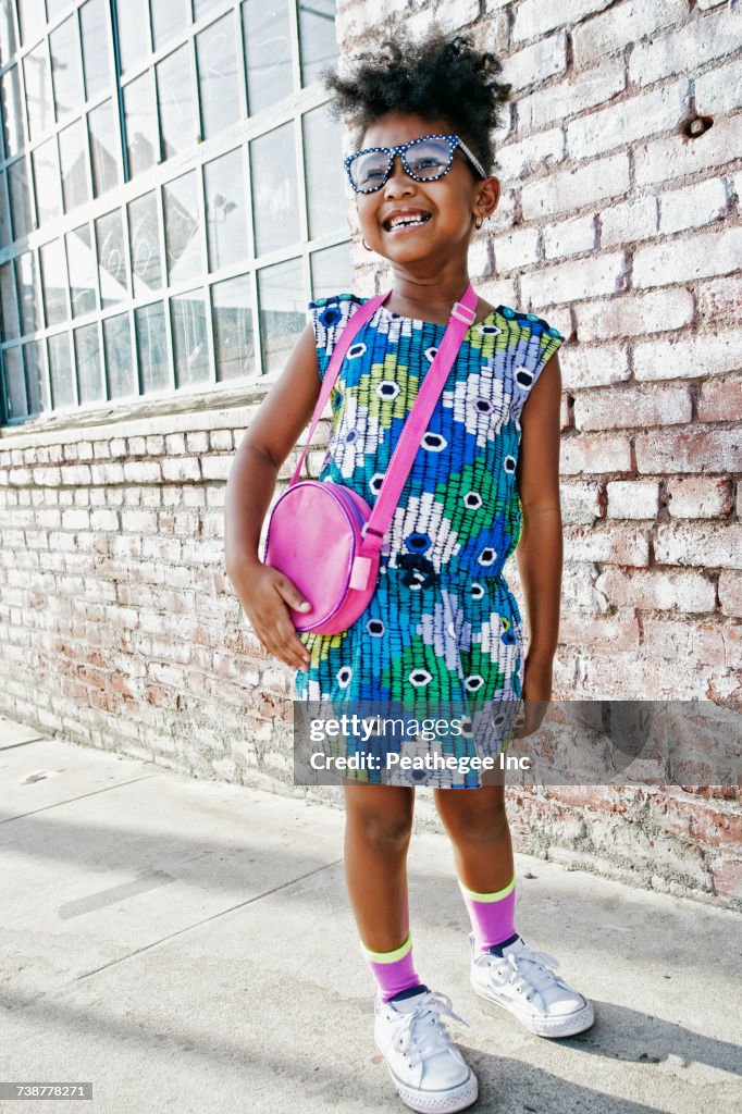 Smiling Black girl standing on sidewalk wearing dress and purse