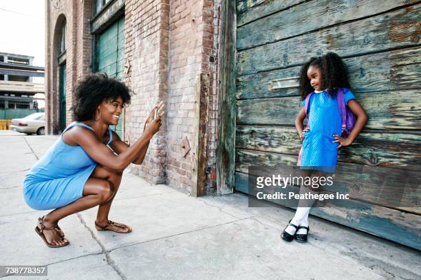 black mother photographing daughter on sidewalk with cell phone - knee length stock pictures, royalty-free photos & images