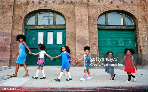 woman leading girls holding hands on city sidewalk - city life authentic stockfoto's en -beelden