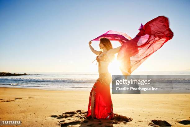 caucasian belly dancer holding scarf on beach - buikdanseres stockfoto's en -beelden