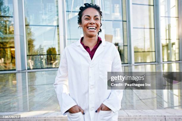 portrait of laughing mixed race doctor outdoors at hospital - doctor white lab coat stock pictures, royalty-free photos & images