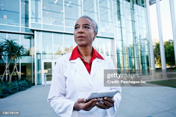 portrait of serious african american doctor holding digital tablet outdoors - medical authority stock pictures, royalty-free photos & images