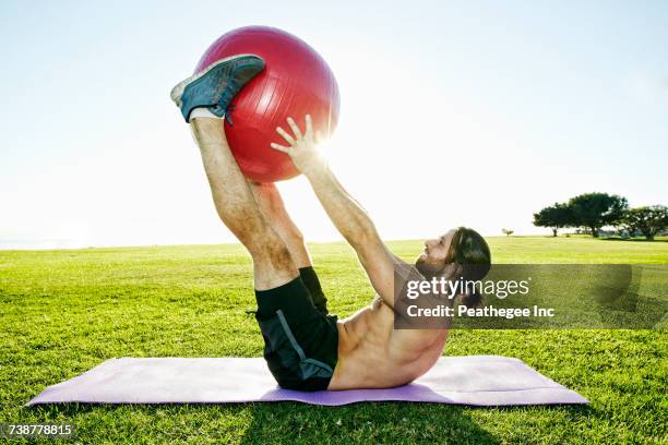 caucasian man lifting fitness ball with legs in sunny field - fitness ball imagens e fotografias de stock