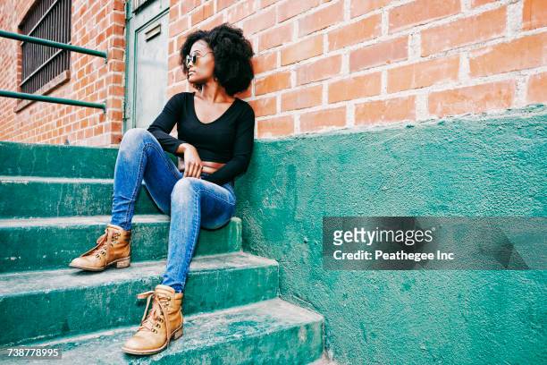 black woman sitting on staircase outdoors - zwarte spijkerbroek stockfoto's en -beelden