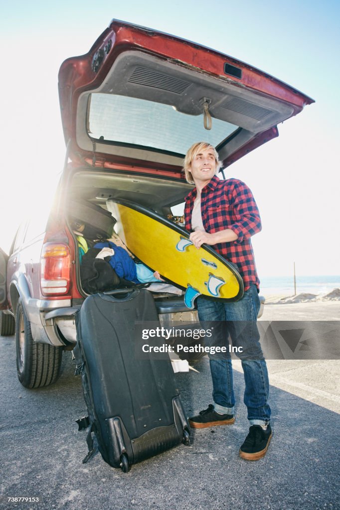 Caucasian man unloading surfboard from car hatch