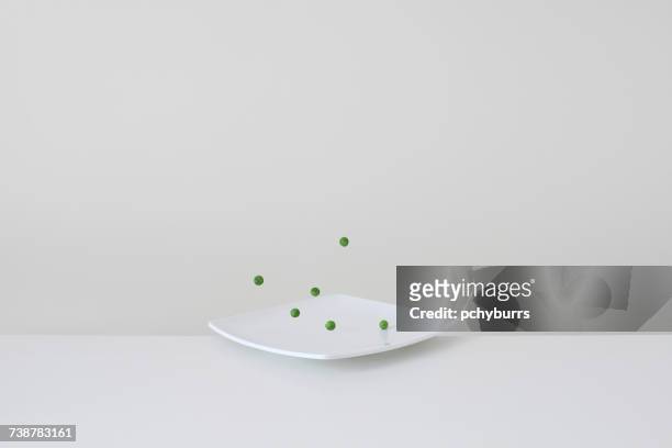 conceptual green peas bouncing on plate - pchyburrs stock pictures, royalty-free photos & images