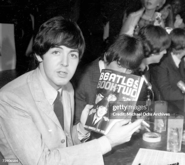 Paul McCartney of the rock and roll band "The Beatles" poses for a portrait during a press conference holding a fanzine entitled "The Beatles Book...