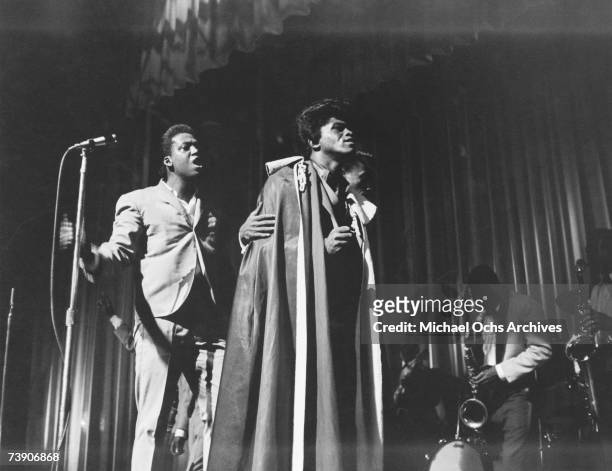 Soul singer James Brown wears a cape as he is led offstage by MC Danny Ray and a member of the Famous Flames at the Apollo Theatre in 1964 in New...