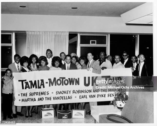 Photo of performers and staff members of Motown Records as they pose in an airport with a sign that reads, in part, 'Tamla-Motown UK Tour,' March...