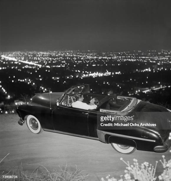 Couple cuddles up in a convertible overlooking Los Angeles from Mulholland Drive at night on July 15, 1951 in Los Angeles, California, Hollywood.