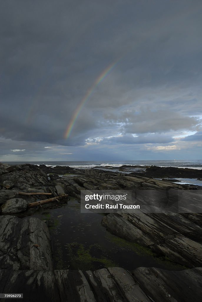 Cape Elizabeth, Maine. Churning surf on the rocky coast and a rainbow under stormy clouds.