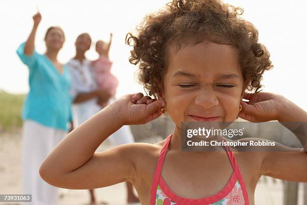 girl (3-4) with fingers in ears, head and shoulders, with family behind - fingers in ears 個照片及圖片檔