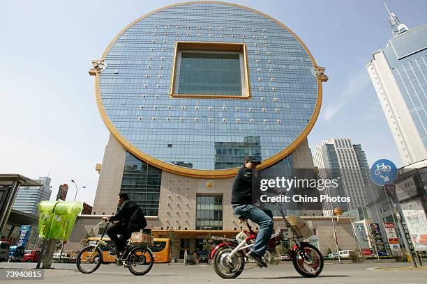 People pedal past a building shaped as a Chinese ancient coin on April 21, 2007 in Shenyang of Liaoning Province, China. China reported a 13 percent...