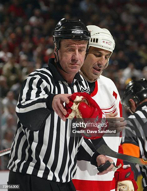 Linesman Pat Dapuzzo grabs the glove of Chris Chelios of the Detroit Red Wings as Chelios looks at his finger during a break in NHL game action...
