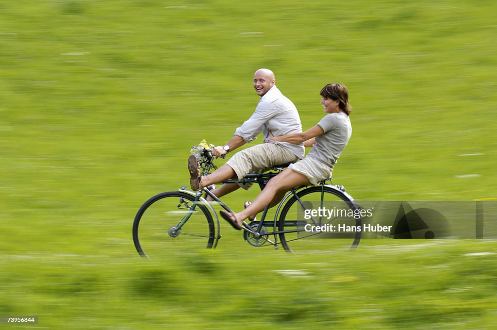 Couple riding bicycle in meadow, side view