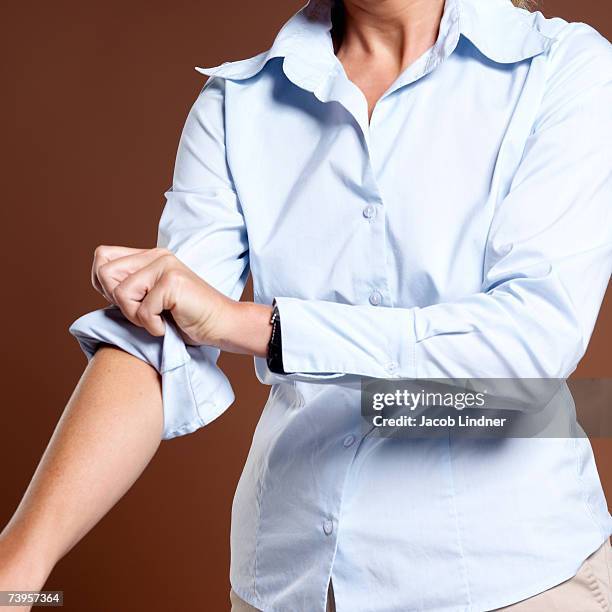 businesswoman rolling up shirt sleeves, close-up - rolling foto e immagini stock