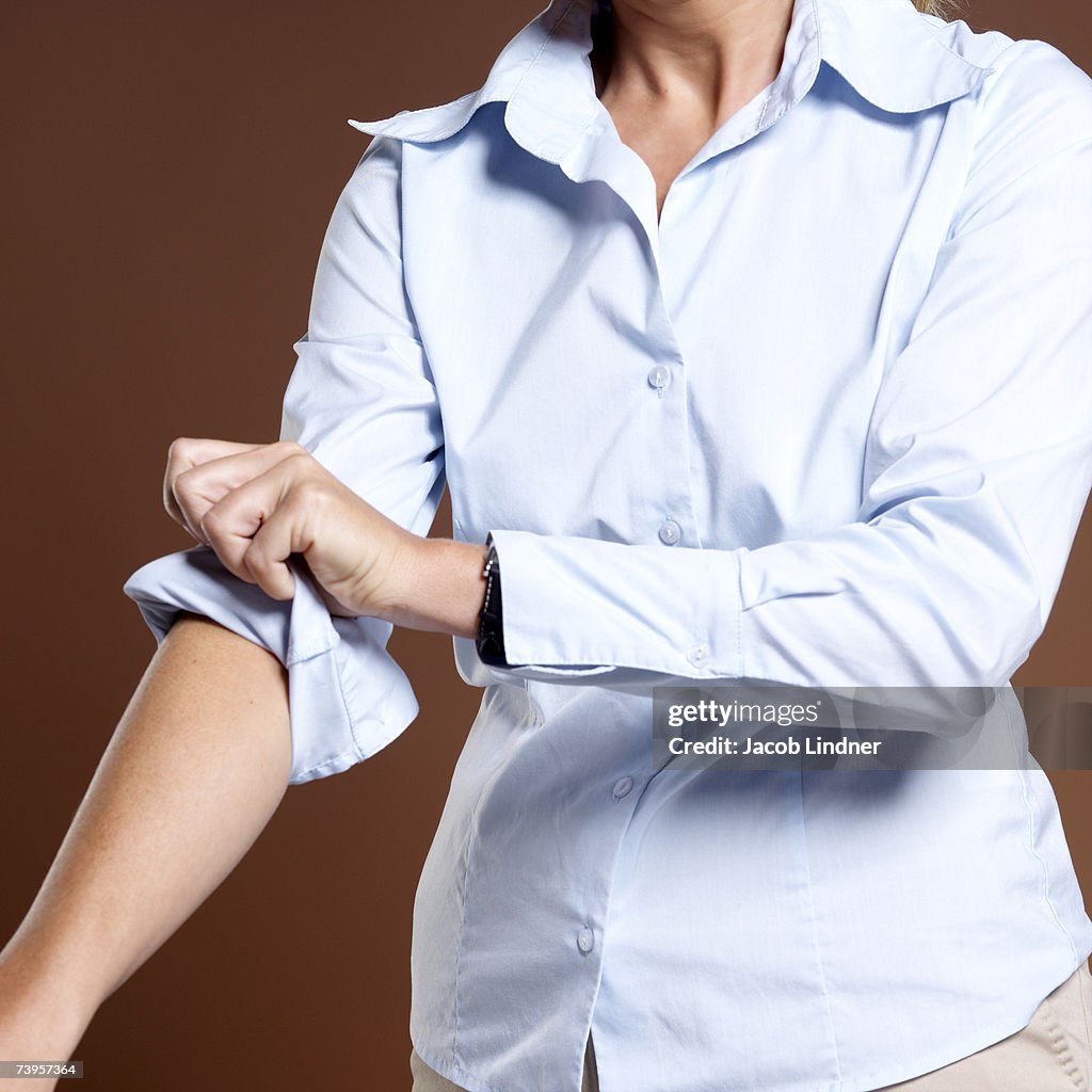 Businesswoman rolling up shirt sleeves, close-up