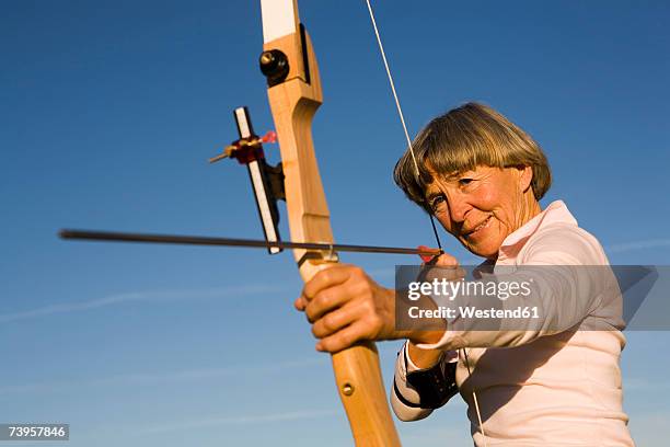 senior adult woman using bow and arrow - bow and arrow stock pictures, royalty-free photos & images