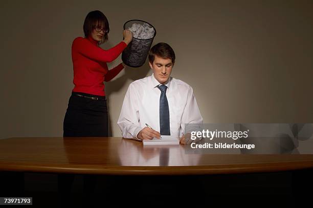 young businesswoman emptying wastebasket over her colleague - business revenge stock pictures, royalty-free photos & images