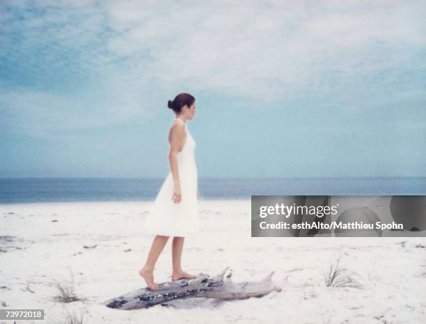 young woman standing on driftwood on beach, side view - white dress stock pictures, royalty-free photos & images
