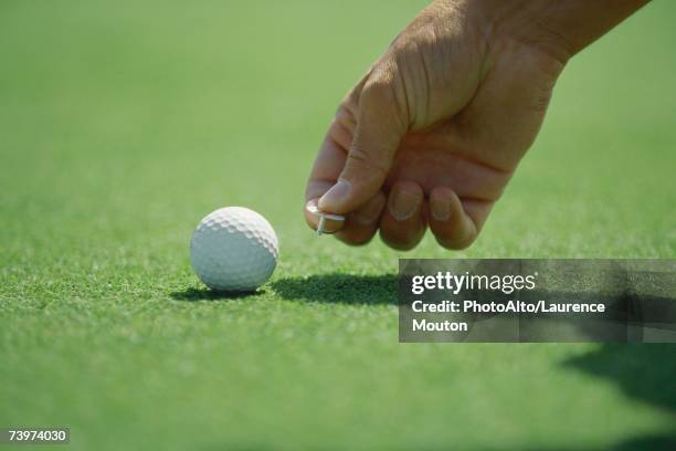 golfer placing golf ball marker on turf, close-up of hand - platzieren stock-fotos und bilder