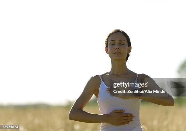 woman standing with hands on chest and stomach, eyes closed - chakras stock pictures, royalty-free photos & images