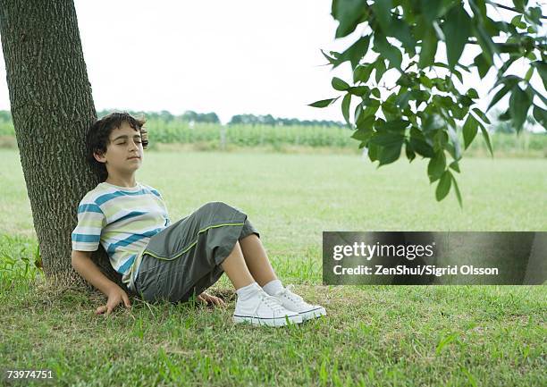 boy sitting on ground, leaning against tree trunk - under value stock pictures, royalty-free photos & images