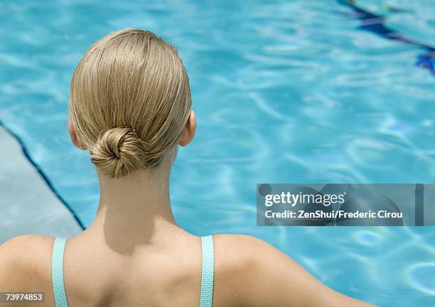 young woman, rear view of head and shoulders, pool in background - haarknoten stock-fotos und bilder
