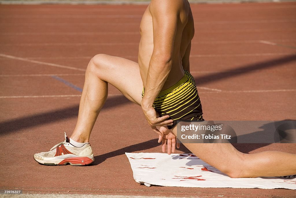 Male athlete stretching on the edge of a running track