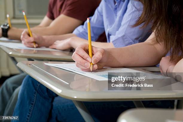 students sitting at desks and writing - examen fotografías e imágenes de stock