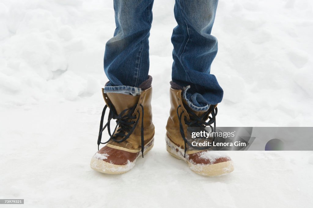 Man standing in unlaced snowboots in snow, low section