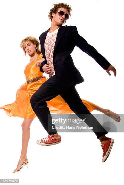 young couple in alternative evening wear skipping in air - arm in arm stockfoto's en -beelden