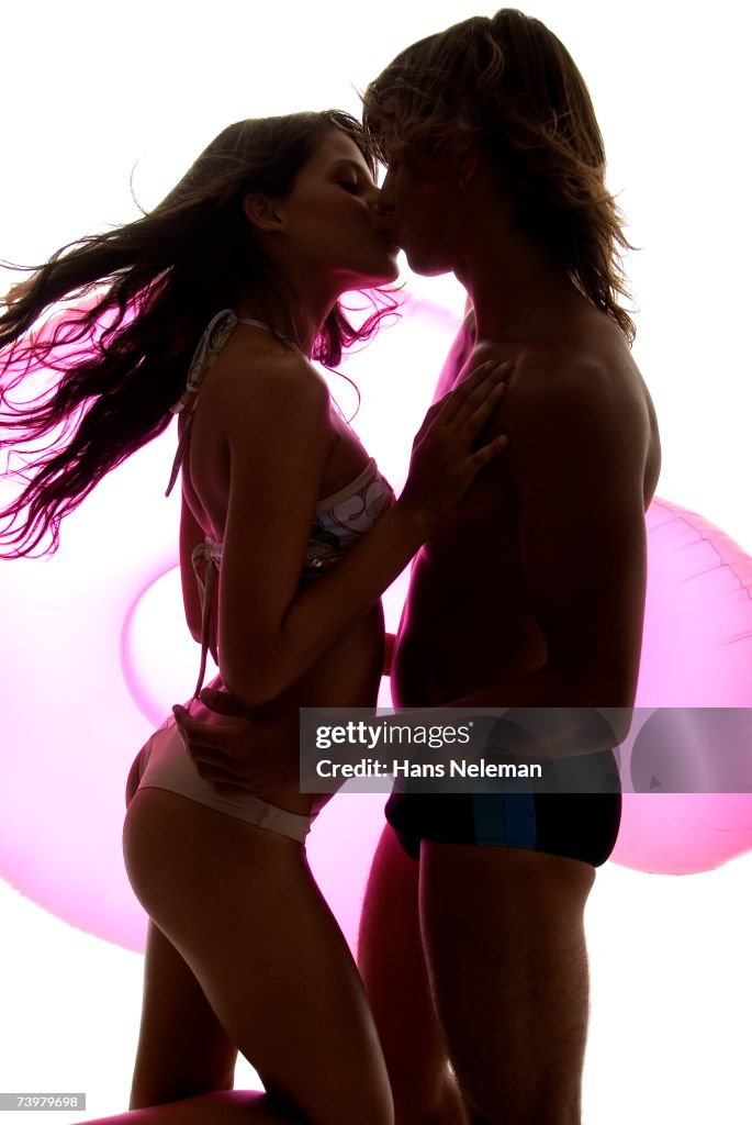 Young couple in swimwear embracing with pink inflatable